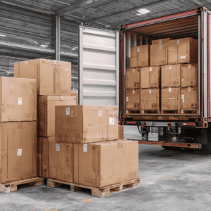 A warehouse scene showing a truck being loaded with stacked cardboard boxes for interstate freight transport.